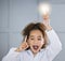 Aha. Cropped portrait of an adorable little girl wearing a labcoat and holding a lightbulb above her head.