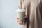 AI generated illustration of a young adult woman holding a hot cup of coffee with lid