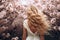 Ai generative. Back view, beautiful young woman with long curly blond hair against the backdrop of cherry blossoms