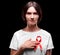 AIDS, awareness concept. A brunette female holding a red ribbon on a black background. Solidarity with people with AIDS.