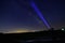 Aiming a flashlight at the Milky way galaxy at night with a farm in the background and light pollution from a nearby town