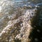 Air bubbles in wavy turbulent water stream on sunshine, abstract water surface