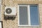 The air conditioner compressor hanging on the wall of a residential building next to the window