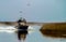 Airboat driving into salt marsh with water spray behind it; man and woman looking ahead, blue sky and birds over head