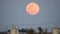 An aircraft approaching Haneda International airport crossing in front of the rising full moon in wi