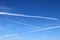 Aircraft condensation contrails in the blue sky inbetween some clouds