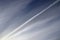 Aircraft condensation contrails in the blue sky inbetween some clouds