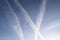 Aircraft condensation contrails in the blue sky inbetween some clouds