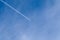 Aircraft condensation contrails in the blue sky inbetween some clouds