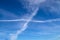 Aircraft condensation contrails in the blue sky inbetween some clouds