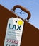 An airline luggage tag hangs from a suitcase or briefcase as an airliner flies high above in the background. This travel tag is fo
