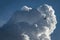 An airplane flies next to a large cumulus cloud before landing at an airport