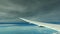 Airplane flight above ocean with clear blue sky and under close heavy dark clouds. Wing of an airplane flying above the white