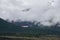 Airplane flying through the clouds over the pine forest covered mountains