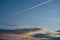 An airplane leaves a white vapor line on a beautiful sunset sky. Blue sky, dark clouds, orange sunset