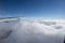 Airplane wing above cloud under clear blue sky.