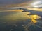 Airplane wing flying over sea and estuary at sunset time. Orange light reflect with ocean. Travel concept.