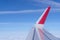 Airplane wing with red colored winglet against blue sky