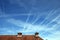 Airplanes tracks sprayed in the sky above a tiled roof.