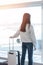 Airport traveller lifestyle of young girl passenger with luggage in airport terminal departure hall area looking out toward