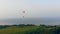 Airsailing vehicle is floating above the water and fields. Skydiver flies in sky.