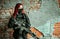 Airsoft red-hair woman in uniform with machine gun beside brick wall