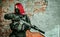 Airsoft red-hair woman in uniform with machine gun beside brick wall inside broken building