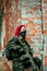 Airsoft red-hair woman in uniform with machine gun standing beside brick wall. Soldier on ruine. Vertical photo