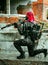 Airsoft red-hair woman in uniform with machine gun standing on knee. Soldier on ruine. Vertical photo side view
