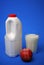 Airtight one gallon milk jug with a red cap, full glass milk and apple.
