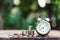 Alarm clock and coin pile on wooden table with blur green garden background, bright morning color tone, finance and business