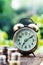 Alarm clock and coin stacks on wooden table with blur green garden background, bright morning color tone, finance and business