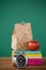 Alarm clock and lunch paper bag with apple on books stack