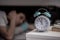 Alarm clock in the morning. Young man tries to sleep in the blurry background, insonmia