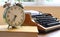 An alarm clock standing on a book against an old typewriter, close-up