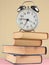 Alarm clock on top of piles of books on pink background.