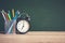 Alarm clock on wooden table on blackboard background in classroom, Back to school concept