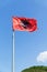 Albania flag against blue sky with white clouds.