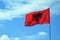 Albanian flag on a flagpole waving on a blue sky