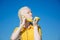 An albino girl in a yellow blouse against a blue sky. pretends to be on the phone. holds a banana and lemon in his hand