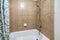 Alcove bathtub with brown ceramic tile surround and patterned shower curtain