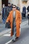 Alex Badia with orange coat and grey jacket and trousers before Giorgio Armani fashion show,