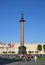 Alexander column on Palace square, covered with natural lawn of green grass and trees on a Sunny day on the background of flags