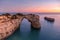 Algarve beach at sunset. Loving moment under natural arch carved in stone is a tourist attraction of the south coast of Portugal.