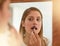 All a woman needs is confidence and a good lipstick. a young woman applying lipstick in front of a mirror at home.