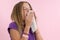 Allergic rhinitis on a summer vacation in a teenage girl`s journey. A girl in a T-shirt on a pink background sneezes into a napki