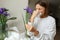 Allergic young woman holds iris flower, covers nose with paper tissue has runny nose, sneezes from flowers pollen at