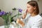 Allergic young woman holds iris flower, covers nose with paper tissue has runny nose, sneezes from flowers pollen at