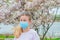 Allergy. Young woman in protective mask from pollen allergy, among blooming trees in park