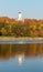 Alley along the riverbank on the background of the autumn park. Tower of the Orthodox Church. Reflections in the water